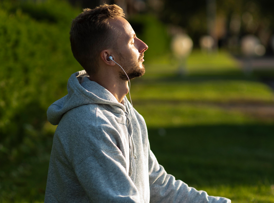 Hombre con capucha y auriculares al aire libre, con expresión serena